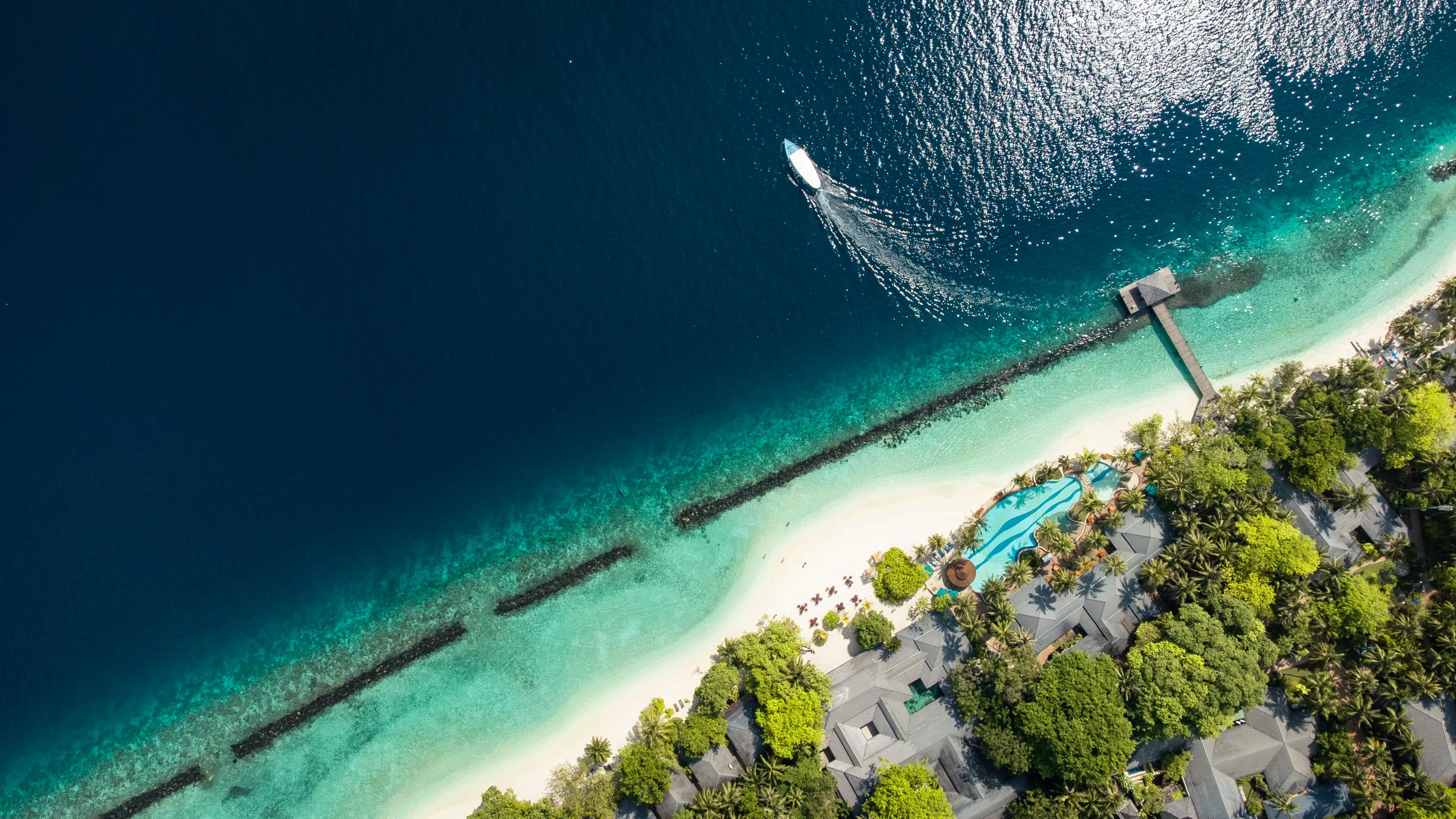 Maledivenküste mit Pool, Boot und türkisblauem Meer aus der Luft