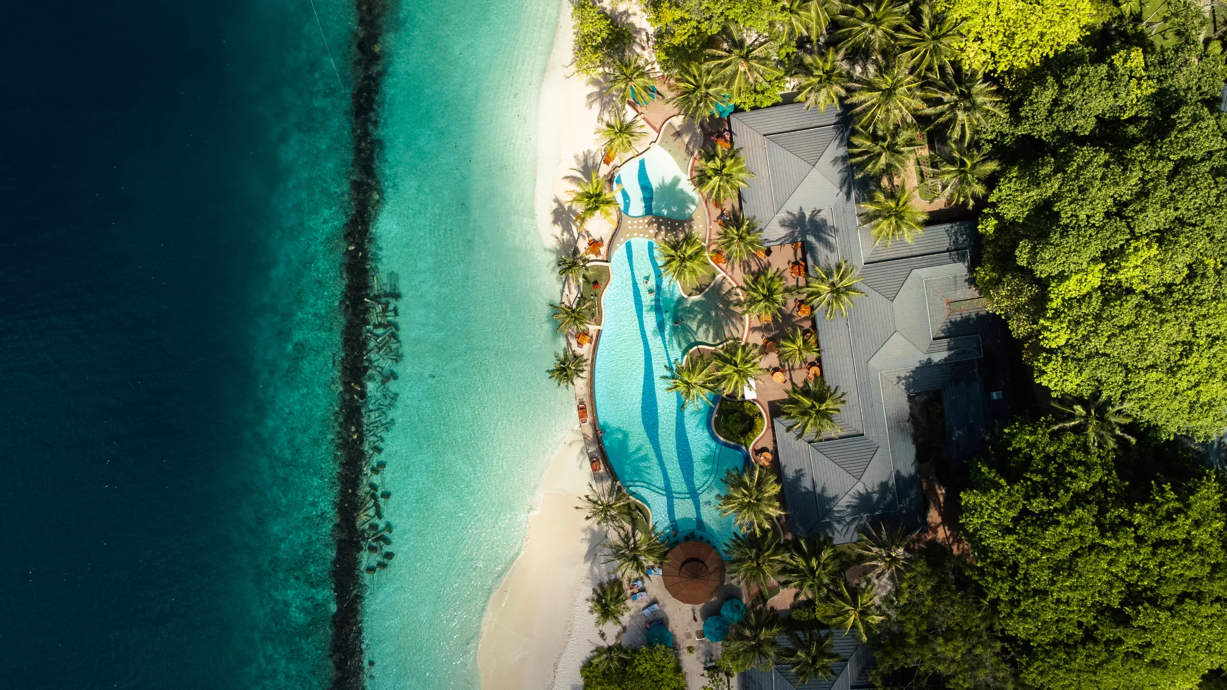 Blick von oben auf Pool, Palmen und Sandstrand auf den Malediven
