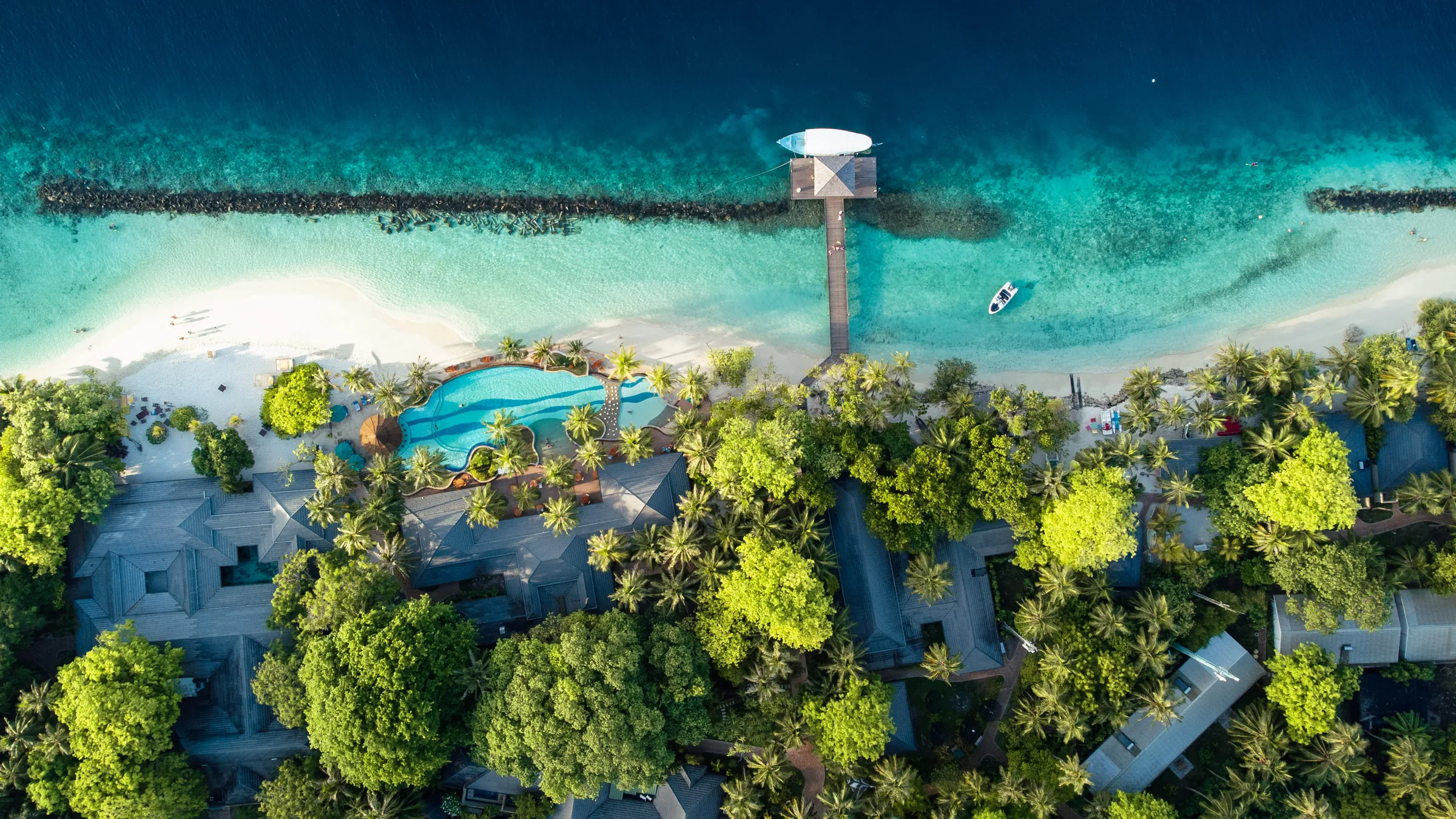 Poolanlage und Bootssteg an einem Maledivenstrand aus der Luft