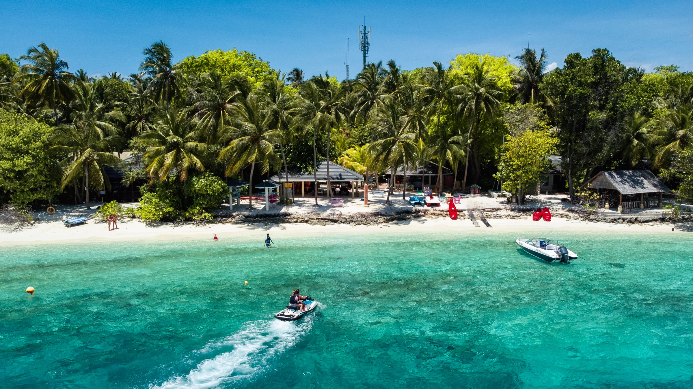 Jetski und Boot vor einem palmengesäumten Strand auf den Malediven